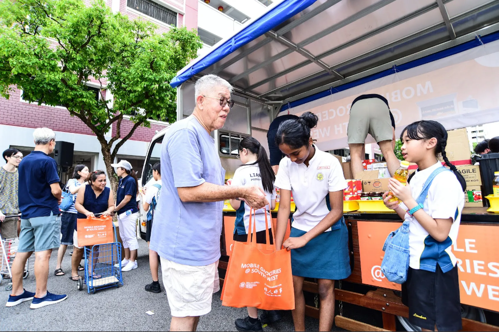 A photo of a student giving an elderly some groceries.
